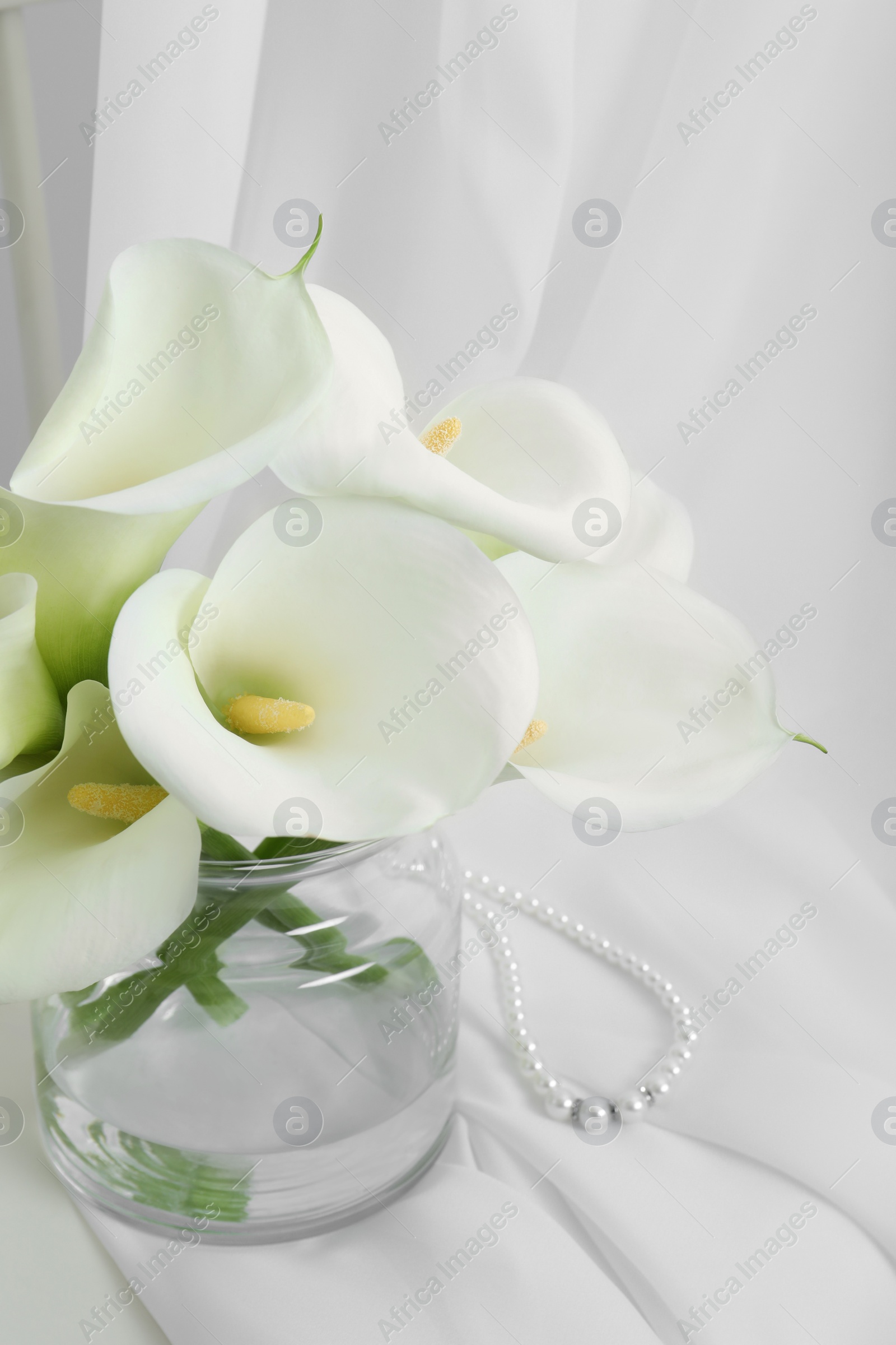 Photo of Beautiful calla lily flowers in glass vase on white cloth
