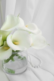 Photo of Beautiful calla lily flowers in glass vase on white cloth