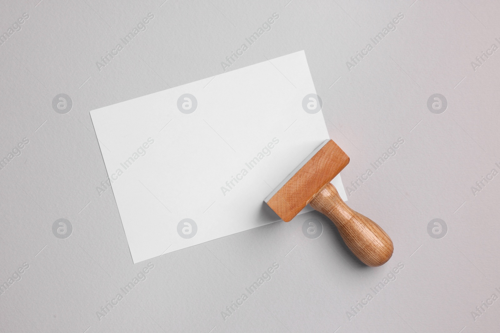 Photo of One wooden stamp tool and sheet of paper on light grey background, top view. Space for text