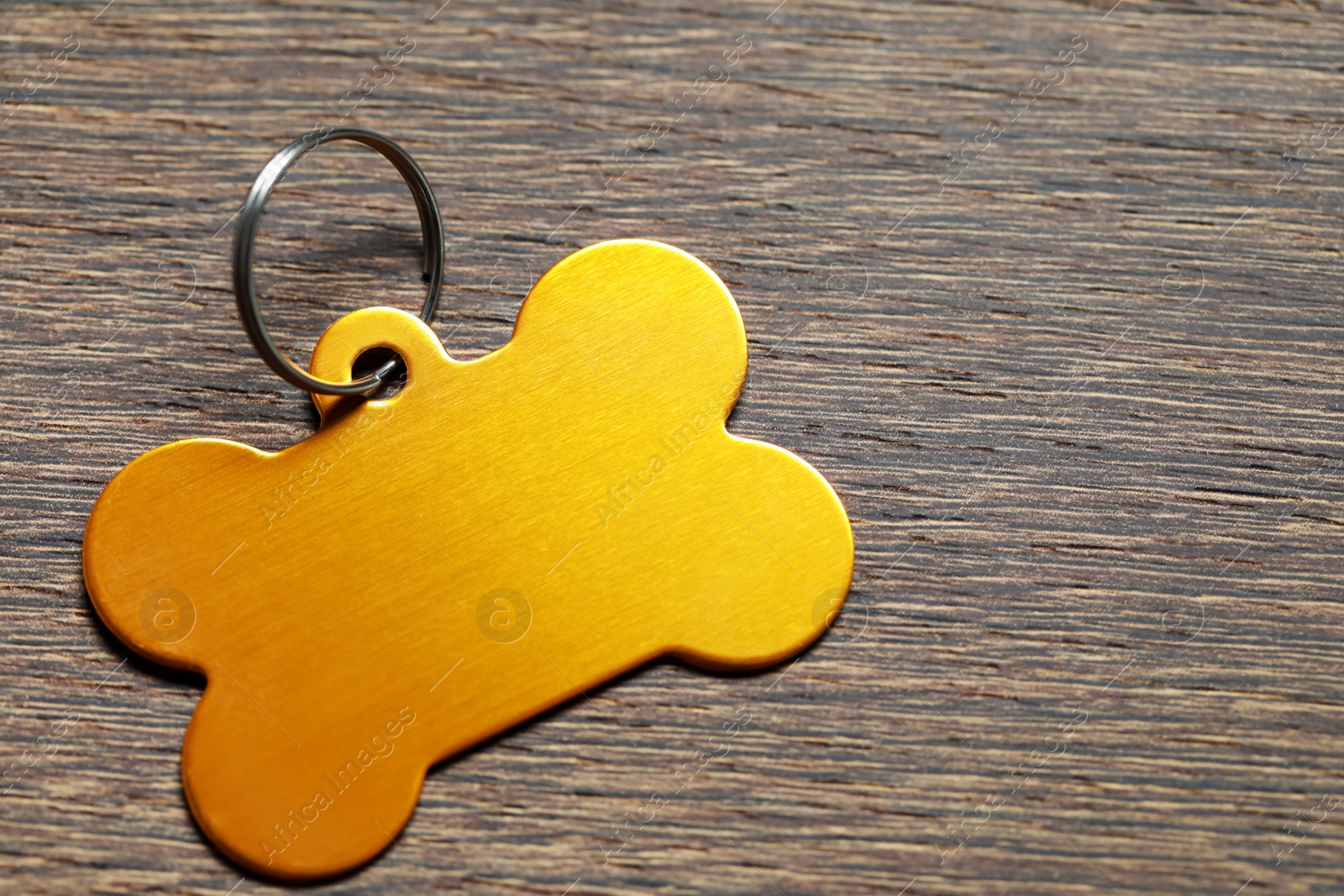 Photo of Yellow metal pet tag in shape of bone on wooden table, closeup. Space for text