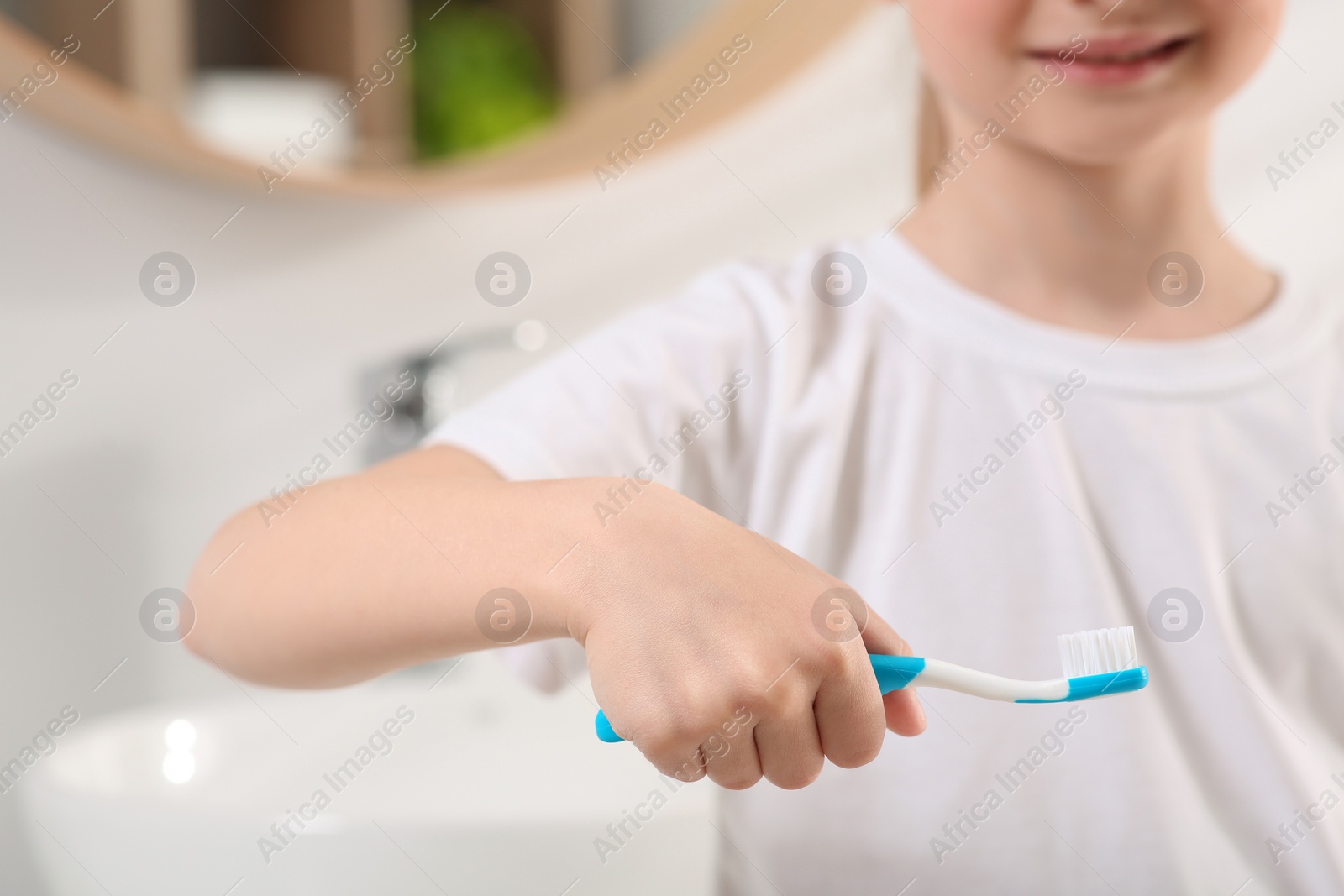 Photo of Little girl holding plastic toothbrush in bathroom, closeup