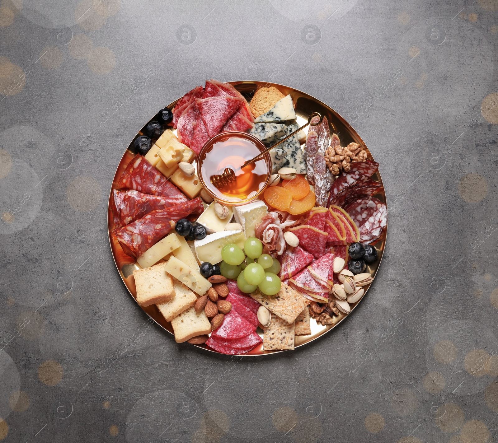 Photo of Plate of different appetizers with honey on grey table, top view. Bokeh effect