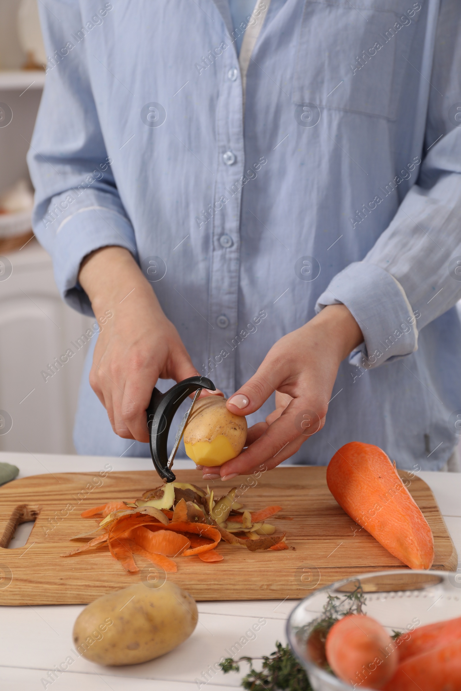 Photo of Woman peeling fresh potato at white wooden table indoors, closeup