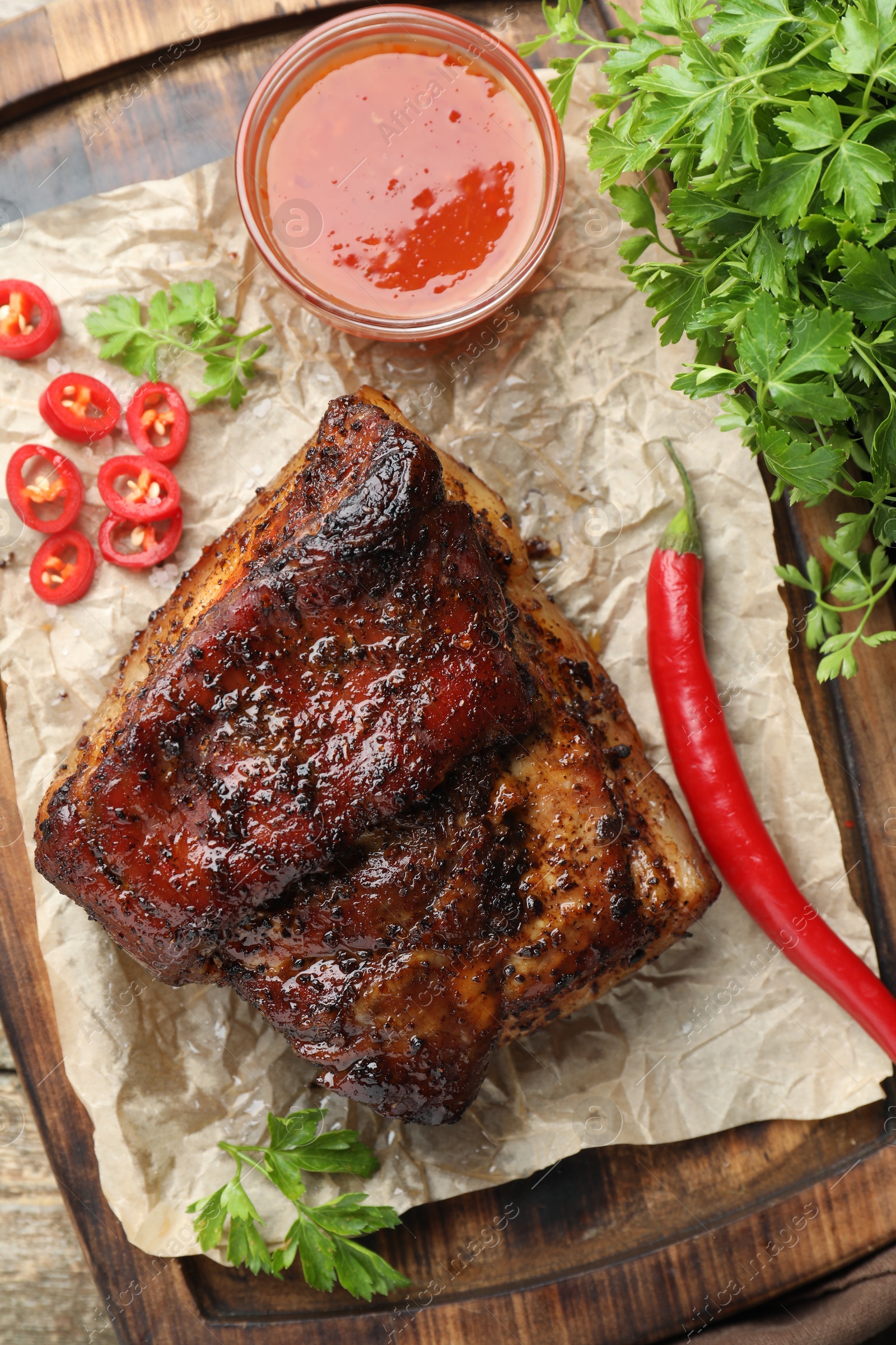 Photo of Piece of baked pork belly served with sauce and chili pepper on wooden table, top view