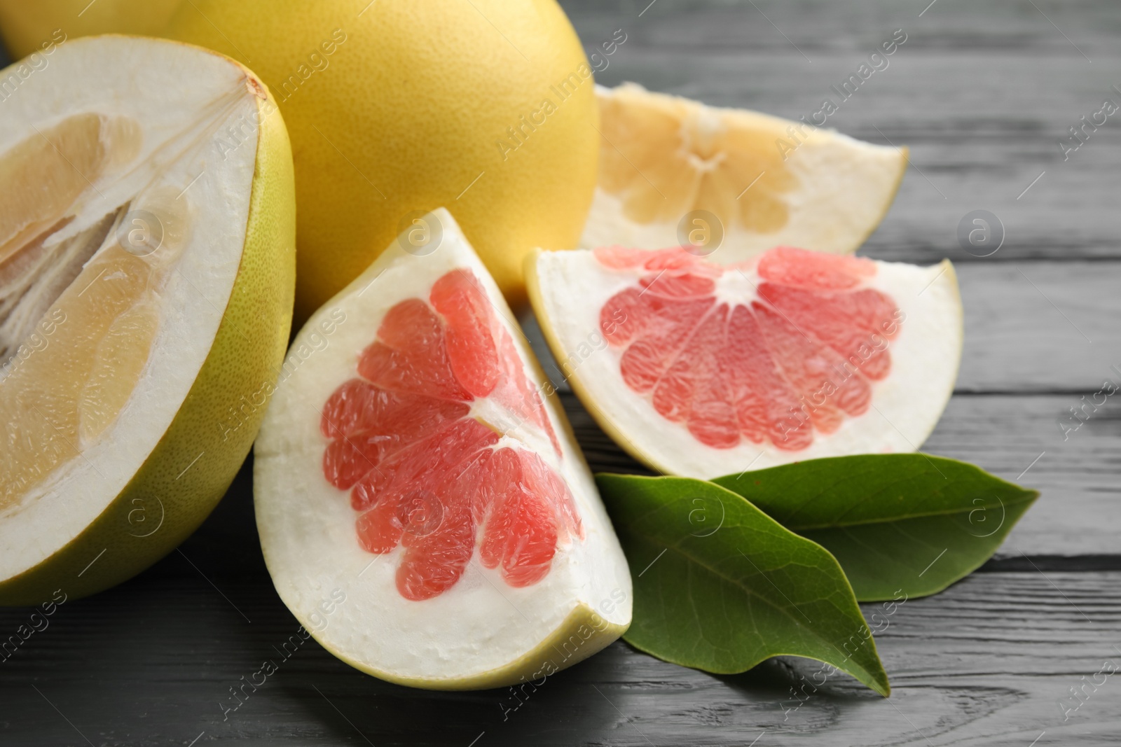 Photo of Fresh cut pomelo fruits with leaves on grey wooden table, closeup