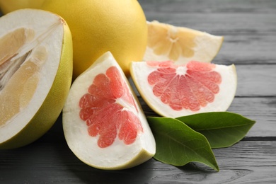 Photo of Fresh cut pomelo fruits with leaves on grey wooden table, closeup