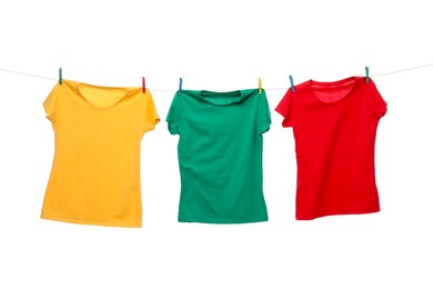 Different bright t-shirts drying on washing line against white background