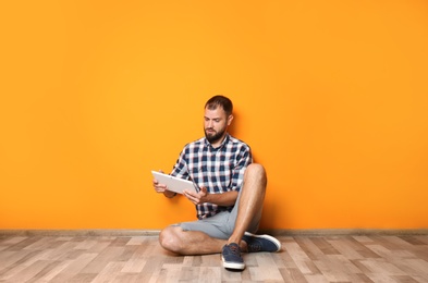 Man in casual clothes with tablet near color wall