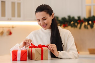 Photo of Smiling woman opening Christmas gift at table in room