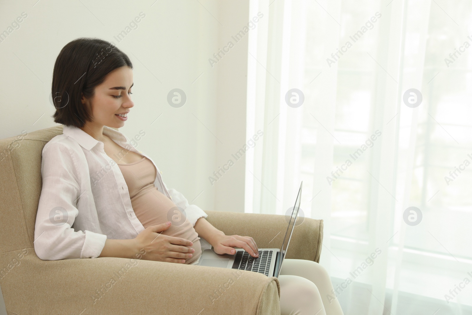 Photo of Pregnant young woman with laptop at home, space for text