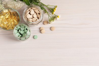 Different pills, flowers and herbs on white wooden table, flat lay with space for text. Dietary supplements