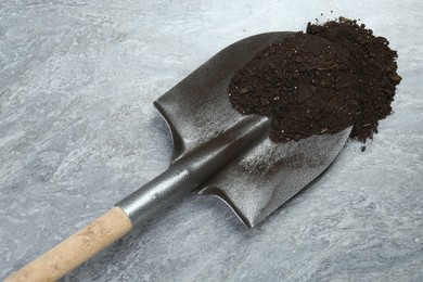 Photo of Metal shovel with fertile soil on gray textured surface, top view