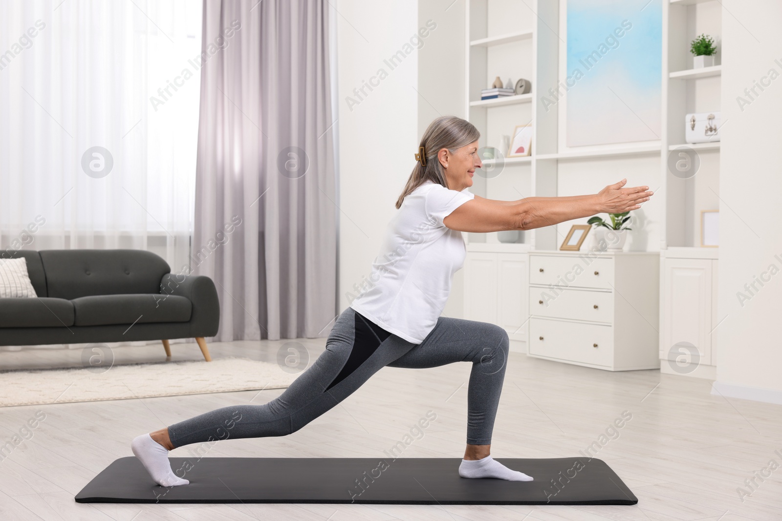 Photo of Happy senior woman practicing yoga on mat at home