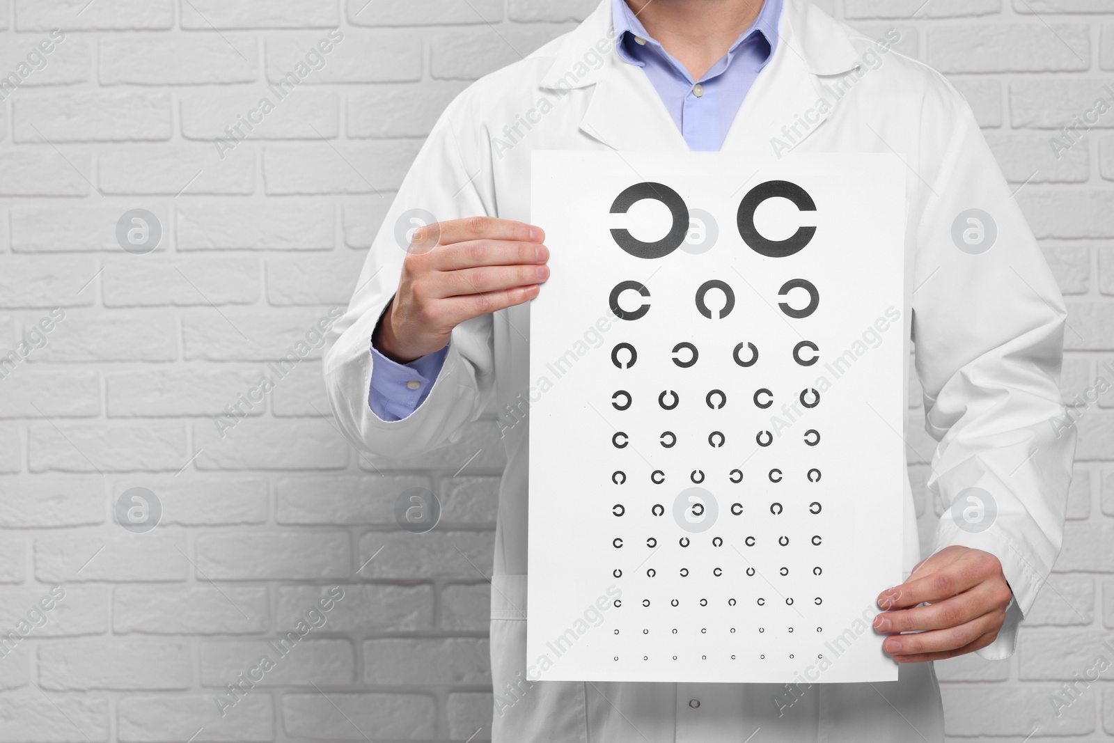 Photo of Ophthalmologist with vision test chart near white brick wall, closeup