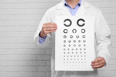 Ophthalmologist with vision test chart near white brick wall, closeup