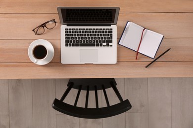 Photo of Chair near wooden table with laptop, cup of coffee and stationery indoors, top view