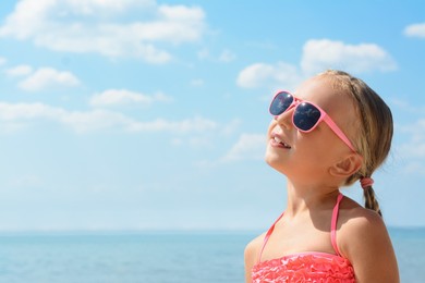 Little girl wearing sunglasses at beach on sunny day. Space for text