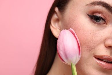 Beautiful woman with fake freckles and tulip on pink background, closeup. Space for text