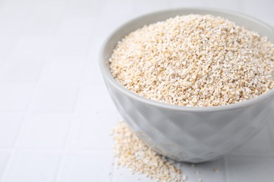 Photo of Dry barley groats in bowl on white tiled table, closeup. Space for text