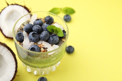 Photo of Tasty chia matcha pudding with coconut and blueberries on yellow background, space for text. Healthy breakfast