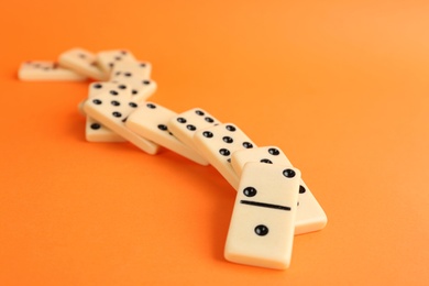 Photo of Fallen white domino tiles on orange background