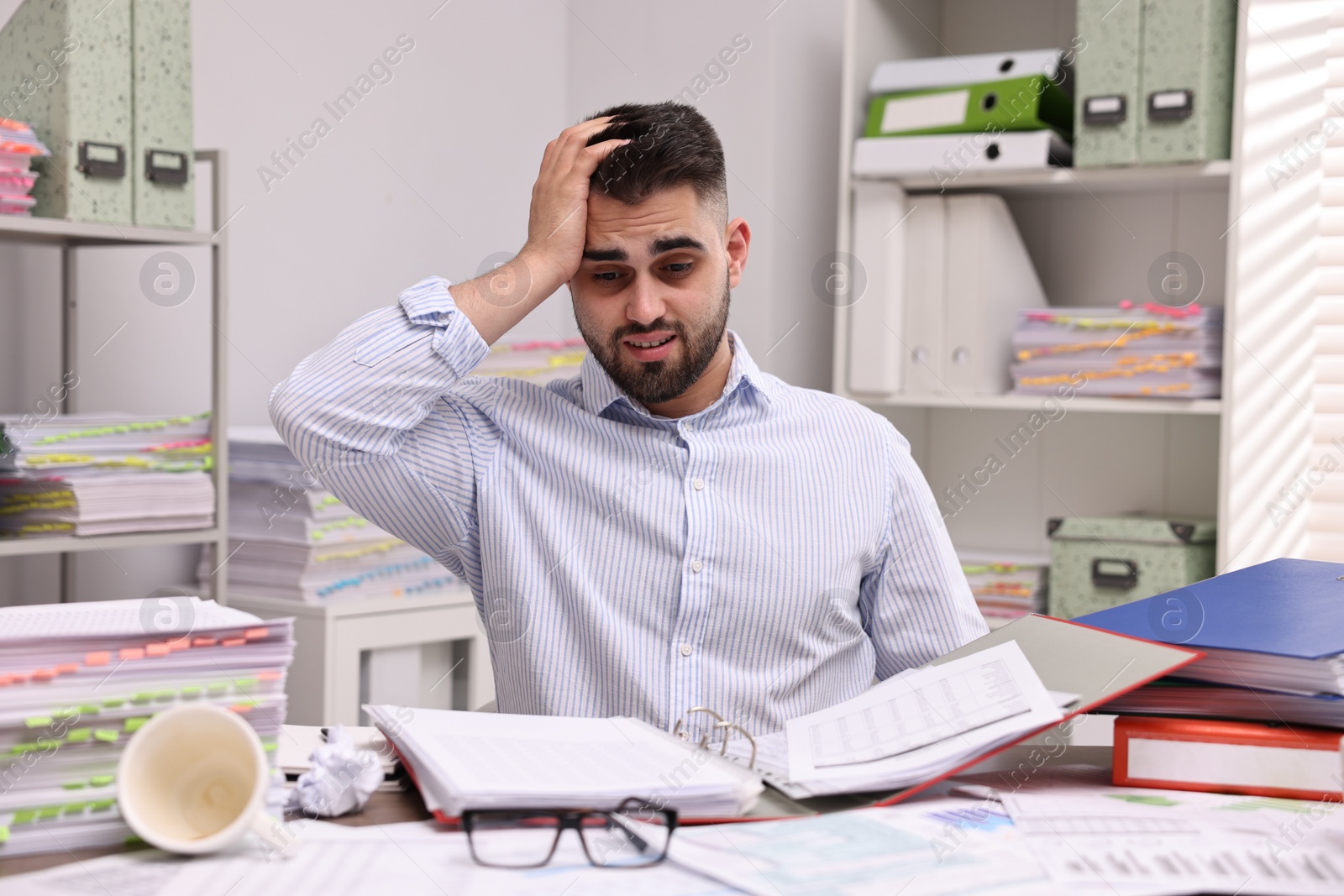 Photo of Overwhelmed man surrounded by documents at workplace in office