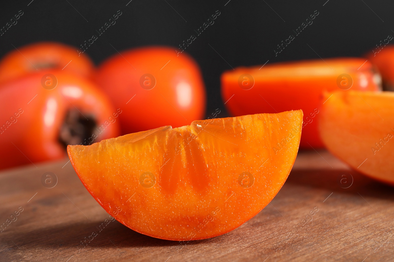 Photo of Piece of delicious ripe persimmon on wooden board, closeup