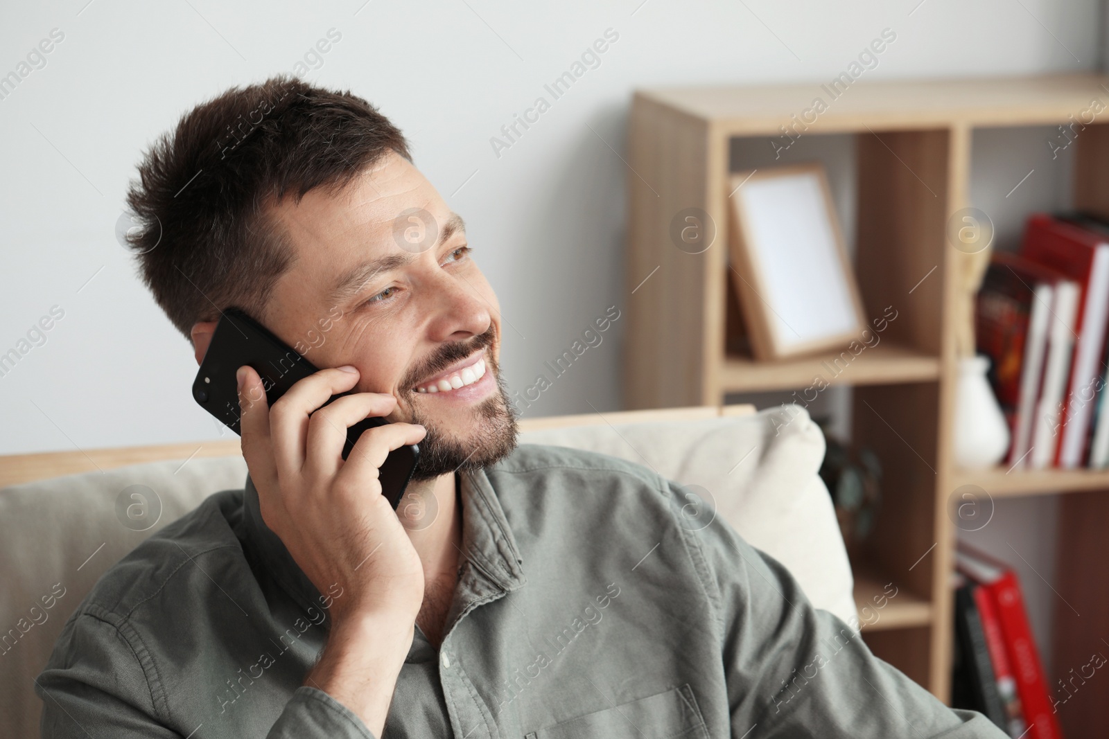 Photo of Happy man talking on smartphone at home