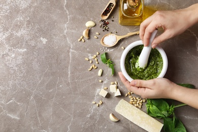 Photo of Woman mixing pesto sauce with pestle in mortar on grey table, flat lay. Space for text