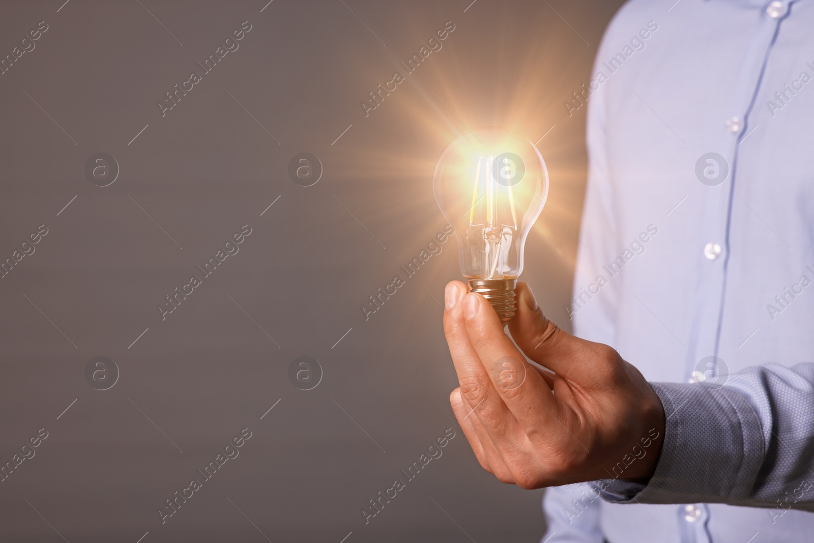 Photo of Glow up your ideas. Closeup view of man holding light bulb on grey background, space for text