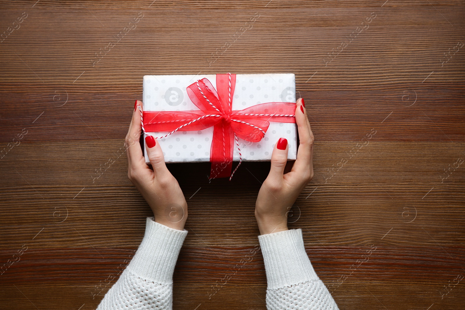 Photo of Woman holding white Christmas gift box at wooden table, top view