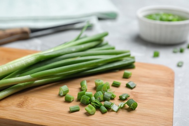 Photo of Wooden board with bunch of fresh green onion on table, closeup