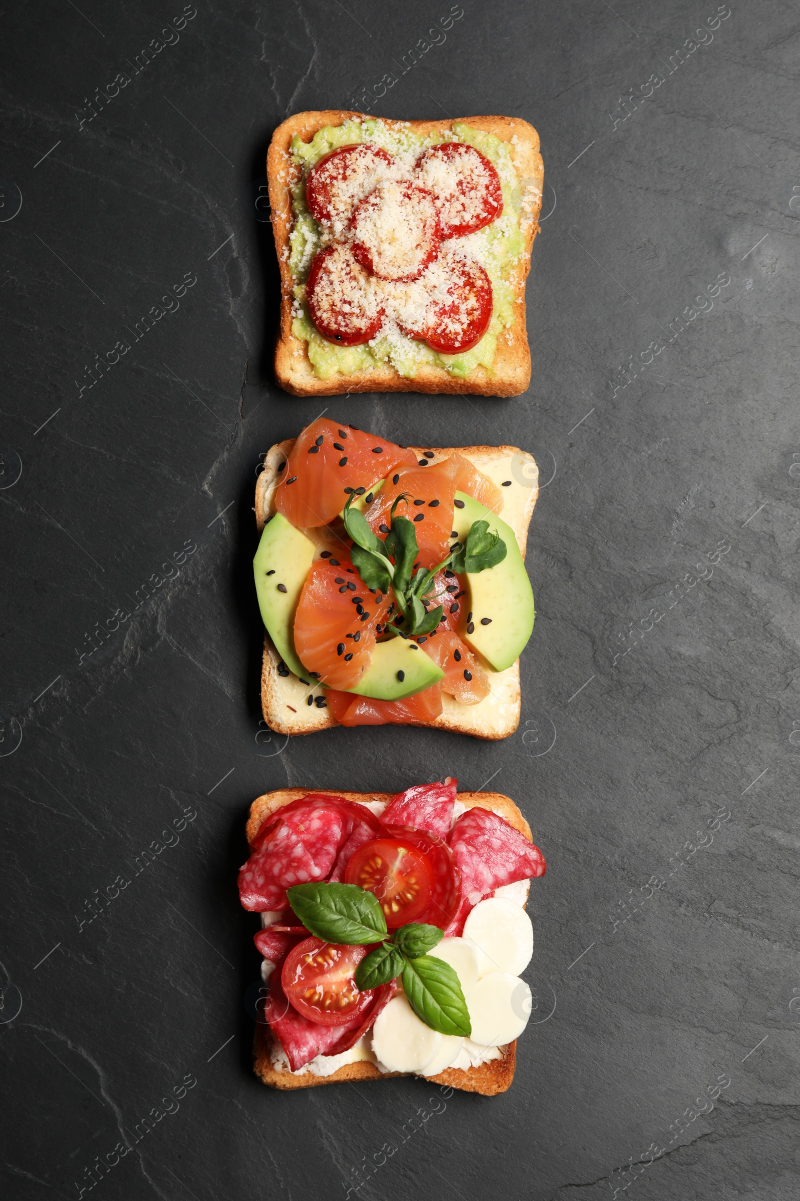 Photo of Tasty toasts with different toppings on black table, flat lay