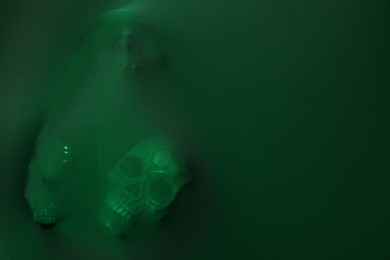 Silhouette of creepy ghost with skulls behind green cloth. Space for text