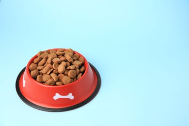 Photo of Dry dog food in feeding bowl on light blue background. Space for text