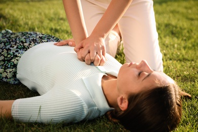 Photo of Woman doing cardiac massage to unconscious person with heart attack on green lawn