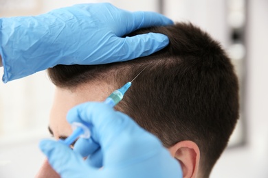 Photo of Young man with hair loss problem receiving injection on blurred background, closeup