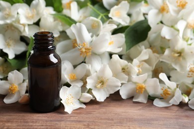 Photo of Jasmine essential oil and fresh flowers on wooden table, space for text