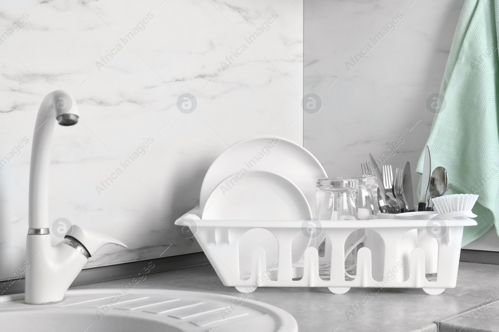 Photo of Drying rack with clean dishes, glasses and cutlery near sink in kitchen