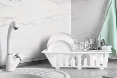 Drying rack with clean dishes, glasses and cutlery near sink in kitchen