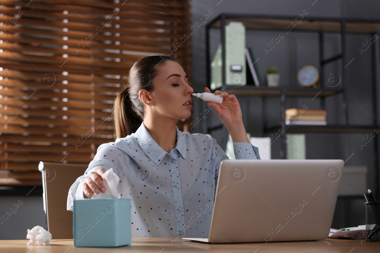 Photo of Ill businesswoman using nasal spray at table in office