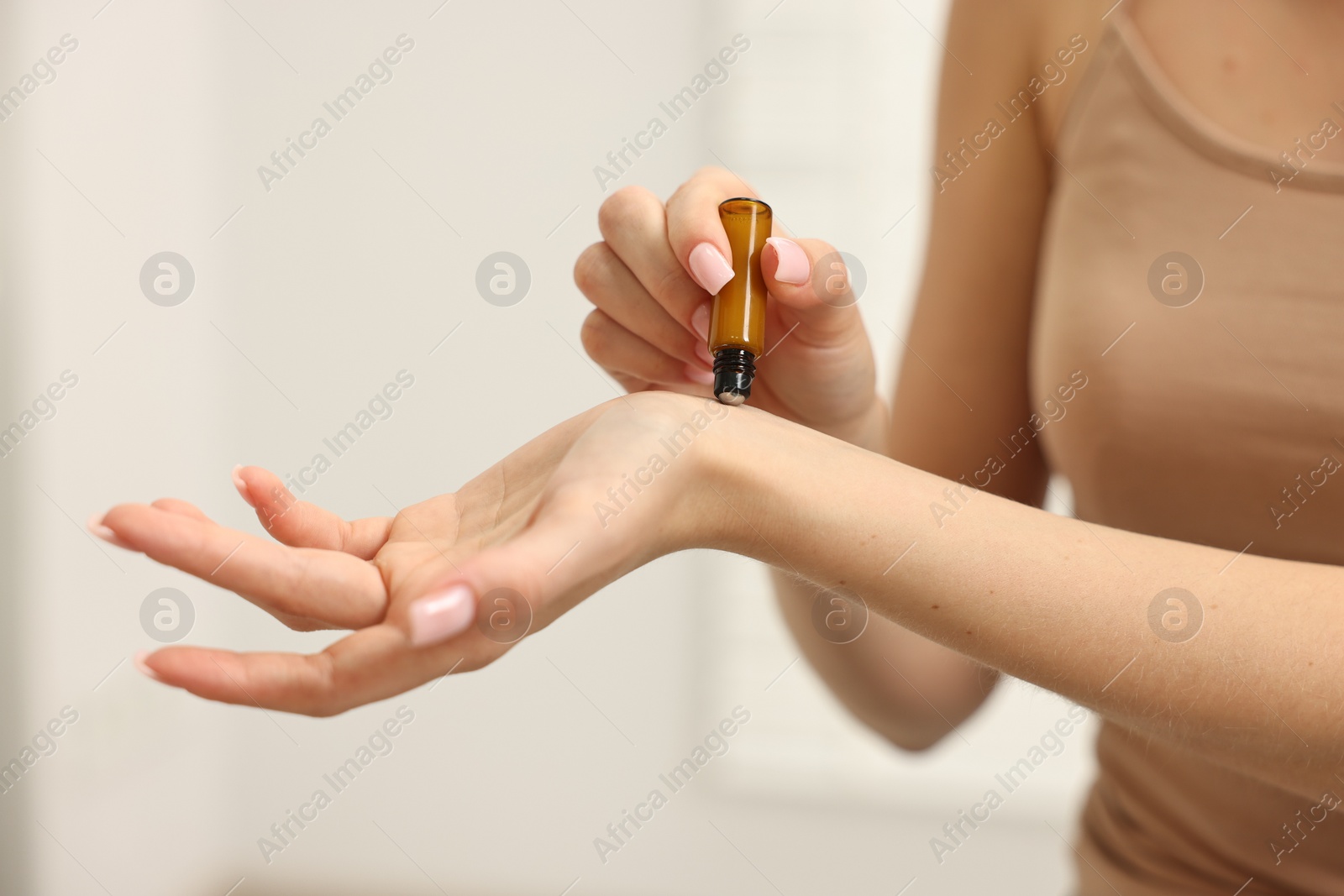 Photo of Aromatherapy. Woman with roller bottle applying essential oil onto wrist against light background, closeup