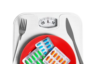 Scales with cutlery and plate full of weight loss pills in blister packs on white background