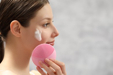 Photo of Young woman washing face with brush and cleansing foam indoors, closeup. Space for text