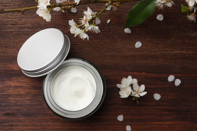 Flat lay composition with jar of face cream and flowers on wooden table. Space for text