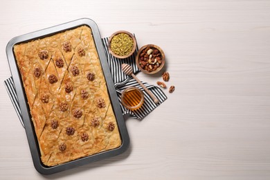 Photo of Delicious baklava with walnuts in baking pan, honey and nuts on white wooden table, flat lay. Space for text