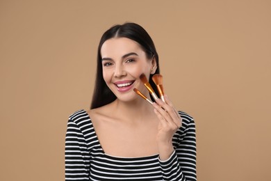 Photo of Happy woman with different makeup brushes on light brown background