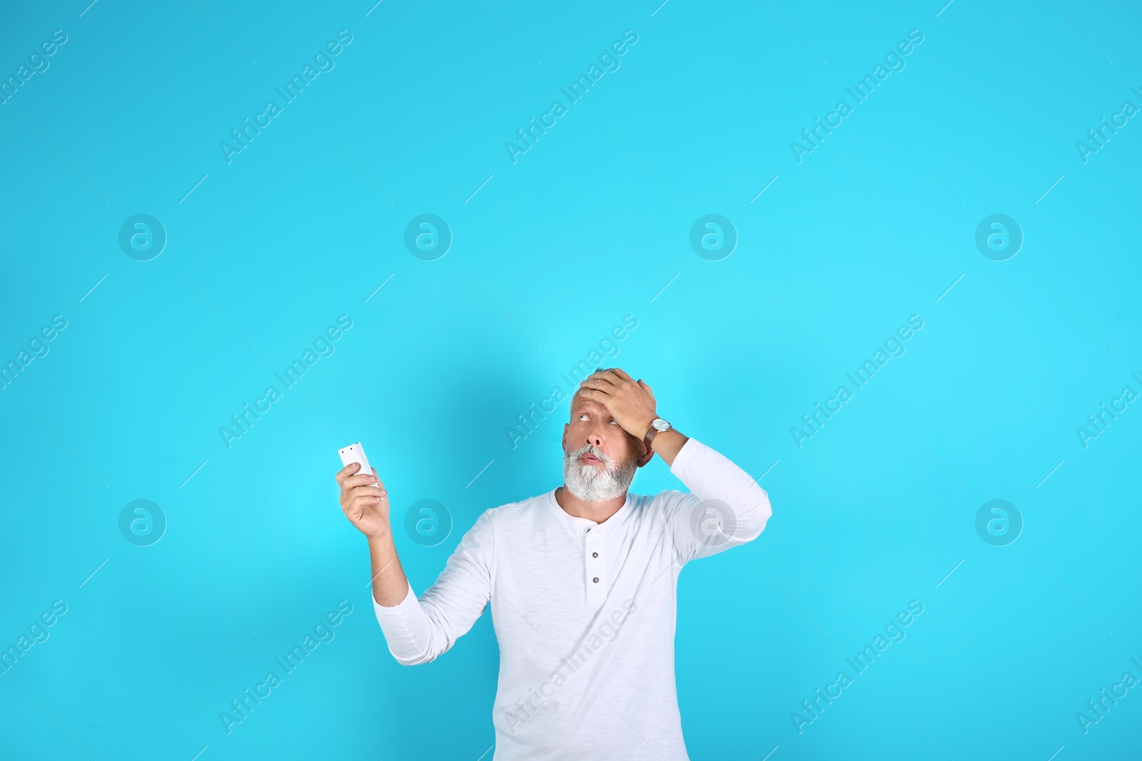 Photo of Senior man with air conditioner remote control suffering from heat on color background