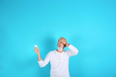 Senior man with air conditioner remote control suffering from heat on color background