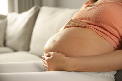 Pregnant woman touching her belly indoors, closeup